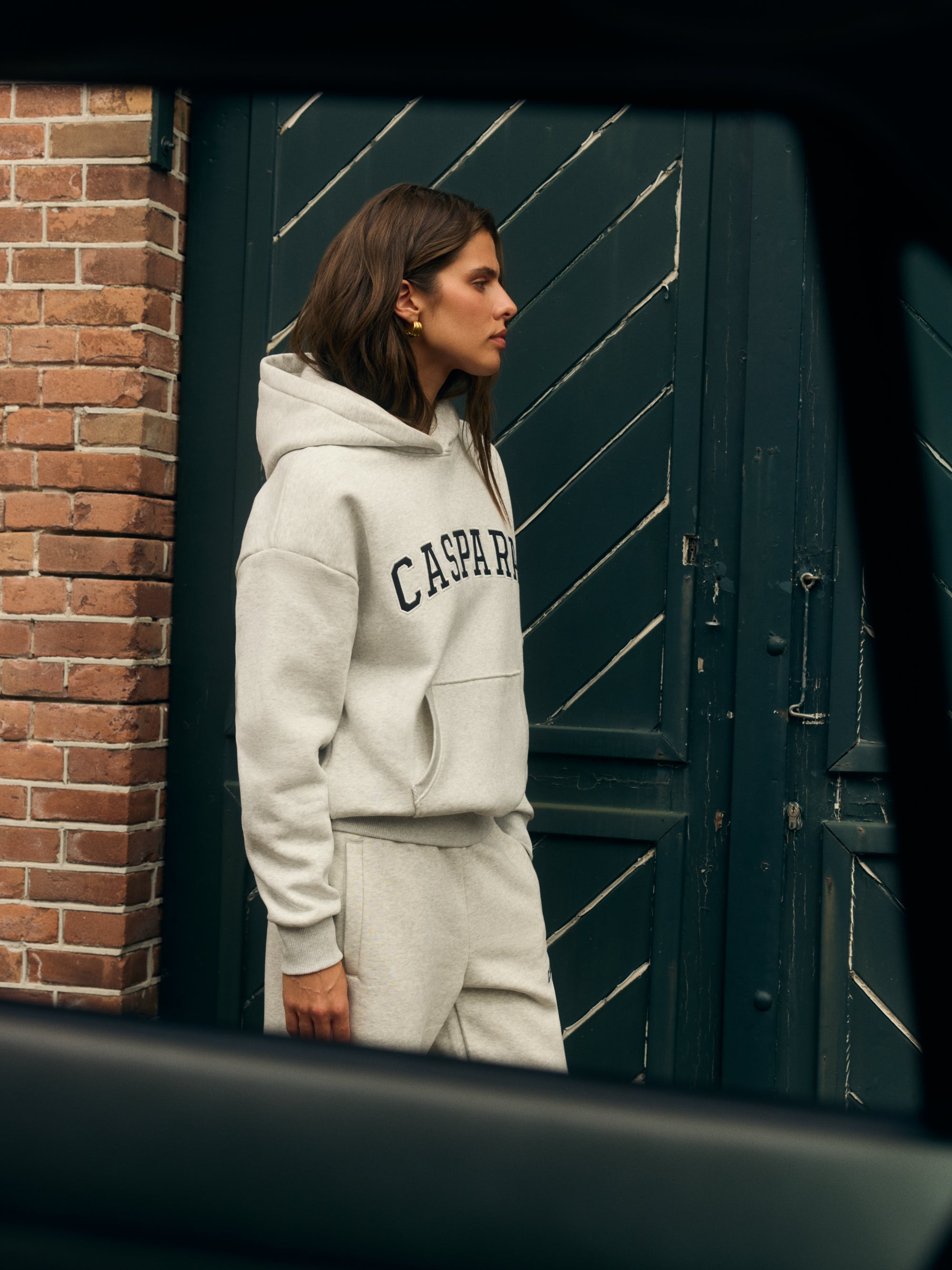 Woman wearing a grey melange CASPARA logo hoodie and matching sweatpants outdoors.